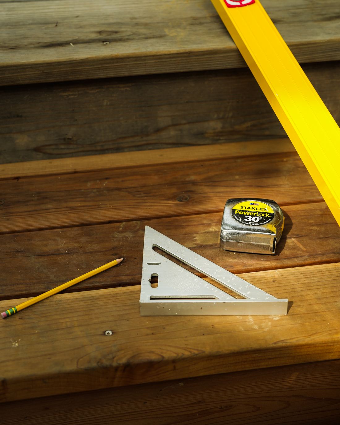 A level, speed square, tape measure and pencil laid out on redwood steps